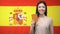 Smiling Asian girl holding passport against Spanish flag background, citizenship