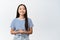 Smiling asian girl looks polite and professional, ready to help and provide assistance, stands against white background