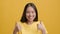 Smiling Asian Lady Gesturing Thumbs-Up With Both Hands, Yellow Background