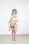 Smiling asian little child girl cuddle a teddy bear doll standing in white room