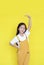 Smiling asian little child girl measures growth by hand isolated over yellow background. Kid estimate her height with looking