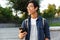 Smiling asian male student in eyeglasses and earphones holding smartphone