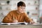 Smiling asian schooler doing homework, writing at notebook