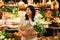 Smiling Asian woman holding wicker shopping basket with vegetables while standing at the farmers market