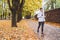 Smiling athletic woman have a jogging in the autumnal city park. Young fitness female smiling and running by the footway covered