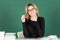 Smiling attractive blonde girl student or woman teacher portrait on green blackboard in classroom at collage or high