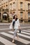 Smiling attractive woman wearing white fashion jacket and jeans look away and cross the street