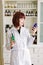 Smiling attractive young lady pharmacist holding green and blue glass bottles in her hands on the background of pharmacy