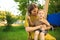 Smiling baby boy and mother ride on swing in playground on green lawn. Summertime photo for ad or blog about motherhood