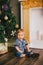 Smiling baby-boy sitting under Chritmas tree near fireplace