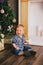 Smiling baby-boy sitting under Chritmas tree near fireplace