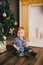 Smiling baby-boy sitting under Chritmas tree near fireplace