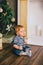 Smiling baby-boy sitting under Chritmas tree near fireplace