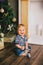 Smiling baby-boy sitting under Chritmas tree near fireplace