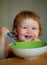 Smiling baby eating food. Funny baby eating food himself with a spoon on kitchen. Healthy nutrition for kids. Launching