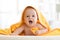 Smiling baby under soft towel. Cute child lying on bed after bathing in living room