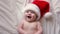 Smiling Baby Wearing Red Santa Claus Hat Celebrating Christmas. Cute Newborn Baby In Christmas Hat Lying On White