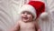 Smiling Baby Wearing Red Santa Claus Hat Celebrating Christmas. Cute Newborn Baby In Christmas Hat Lying On White