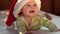 Smiling Baby Wearing Red Santa Claus Hat Celebrating Christmas. Cute Newborn Baby In Christmas Hat Lying On White