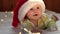 Smiling Baby Wearing Red Santa Claus Hat Celebrating Christmas. Cute Newborn Baby In Christmas Hat Lying On White