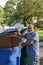 Smiling bald senior citizen man standing in a street with his hands on a recycling can full of cardboard