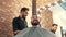 Smiling barber trimming and talking with bearded client in barbershop