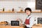 Smiling barista holding signboard with open inscription and looking at camera.