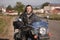 Smiling bearded biker in black leather jacket sitting on modern motorcycle on country roadside.