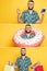 Smiling bearded guy in glasses with donut swim ring, beer, passport and shopping bags on yellow