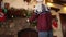 Smiling bearded man in kniited sweater hanging Christmas wreath above fireplace decorated with colorful flashing garland