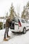 A smiling bearded man puts garbage bags in the trunk of a car, o