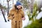 Smiling bearded man wears warm winter clothes and using smartphone with fast internet connection in country side