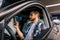 Smiling bearded young man sitting in his car while holding smartphone and reading message. Travel, lifestyle, transport