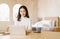 Smiling Beautiful Asian woman in warm clothes work at the laptop computer sitting at desk in bedroom. Positive korean girl