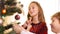 Smiling beautiful girl decorating New Year tree with little boy in living room at home. Portrait of happy Caucasian