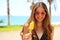 Smiling beautiful girl with sunglasses on the beach eating ice lolly with palm trees on the backgroud. Summer holidays concept