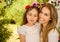 Smiling beautiful mom hugging her pretty daugher in beige dress wearing two red ties in hair