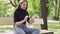 Smiling beautiful woman sitting on bench in green park and using tablet