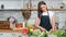 Smiling beautiful young housewife chopping fresh cucumber on cutting board cooking salad at kitchen