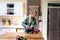 Smiling biracial beautiful young woman with blond hair pouring coffee in mugs on table in kitchen