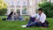Smiling biracial male student sitting on grass and reading interesting book