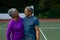 Smiling biracial senior couple embracing and looking at each other while standing in tennis court