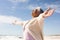 Smiling biracial senior woman enjoying retirement with arms outstretched at beach on sunny day