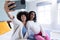 Smiling biracial young woman with afro hair taking selfie with female friend puckering lips at home