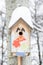 Smiling birdhouse. Birdhouse in the form of a funny face on the tree. Handmade wooden nesting box covered in snow. Winter