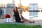 Smiling birthday girl with brown hair in little black dress sitting on the wooden footpath at sunset