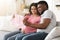 Smiling black expecting couple holding baby clothes