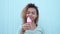 Smiling black girl eating pink melting ice cream in slow motion at blue wall background