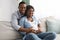 Smiling black man hugging his pregnant woman sitting on sofa