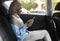 Smiling Black Muslim Female Entrepreneur Browsing Smartphone While Riding Car On Backseat